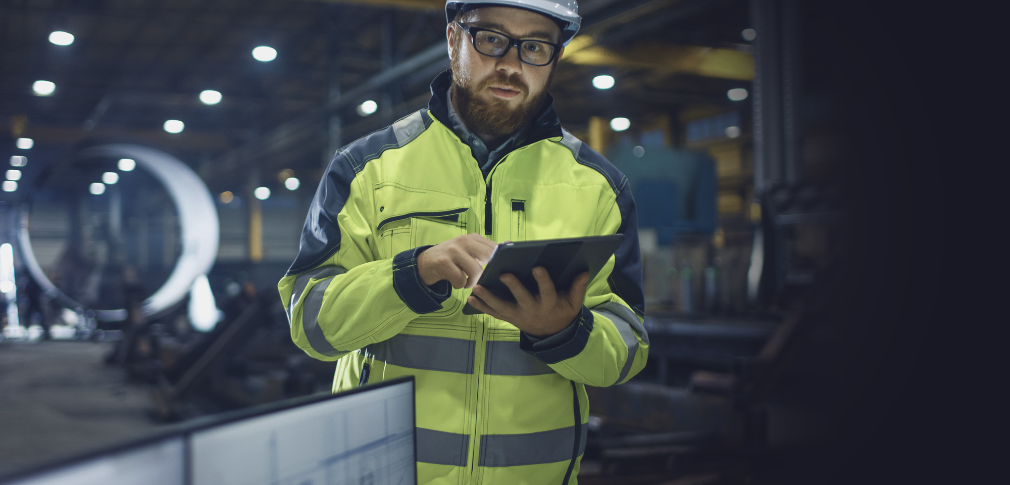 Bearded man holding a tablet in an industrial environment